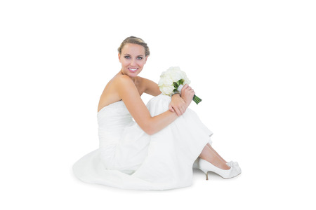 Pretty blonde bride sitting on floor holding a bouquet smiling at cameraの写真素材