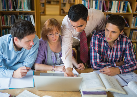 Mature students sitting at the library while looking at teacher use a laptop