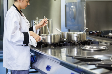 Young chef stirring with ladle in pot in professional kitchenの写真素材