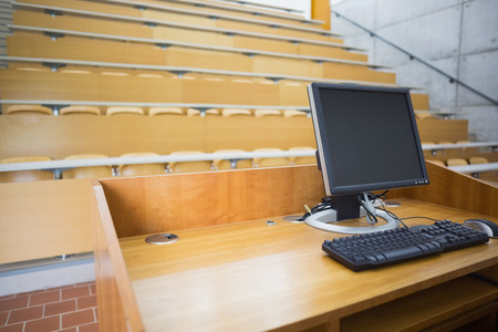 View of computer monitor with empty wooden seats with tables in a lecture hallの写真素材