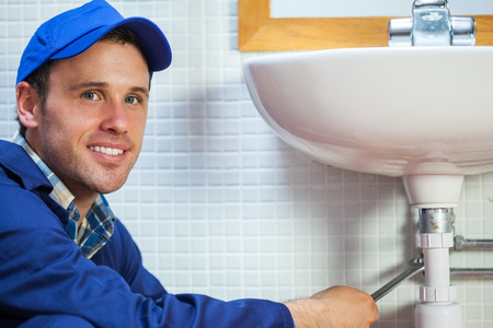 Attractive cheerful plumber repairing sink in public bathroomの写真素材