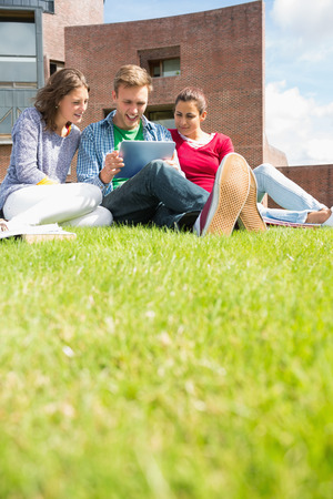 Group of young students using tablet PC in the lawn against college buildingの写真素材