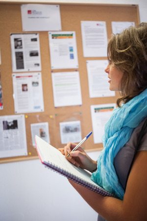 Casual student taking notes in front of notice board in schoolの写真素材