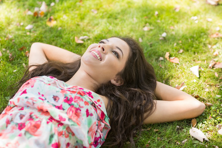 Stylish cheerful brunette lying on the grass in a park on a sunny dayの写真素材