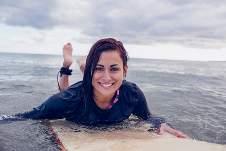 Portrait of a young woman swimming over surfboard in the water at beachの写真素材