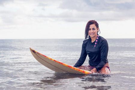 Portrait of a beautiful young woman sitting on surfboard in the water at beach
