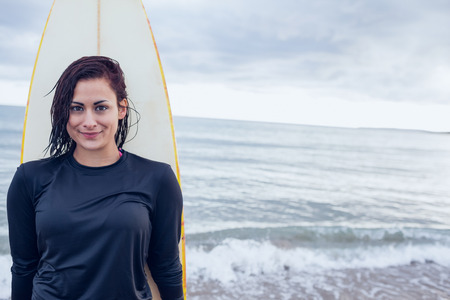 Portrait of a beautiful young woman with surfboard at beachの写真素材