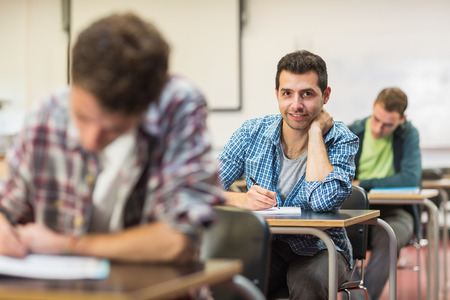 Portrait of a smiling male student with others writing notes in the classroomの写真素材