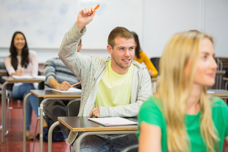Young male student raising hand by others in the college classroomの写真素材