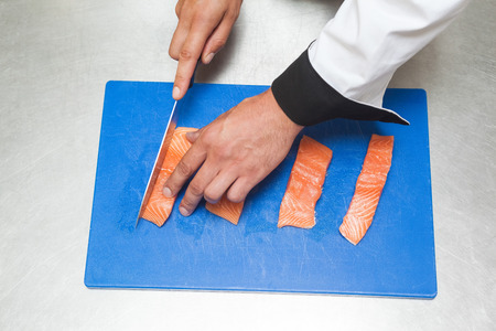Chef slicing raw salmon with sharp knife in professional kitchenの写真素材