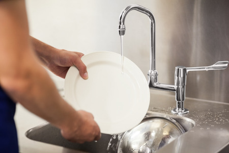Kitchen porter cleaning white plates in sink in professional kitchenの写真素材