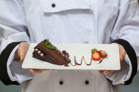 Chef presenting chocolate cake with strawberries on white plateの写真素材