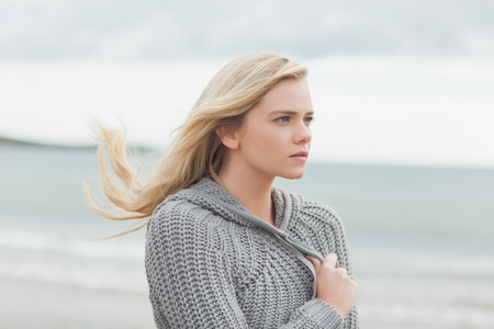 Close up side view of a cute young woman in gray knitted jacket on the beachの写真素材