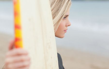 Side view of a beautiful young woman with surfboard on beach