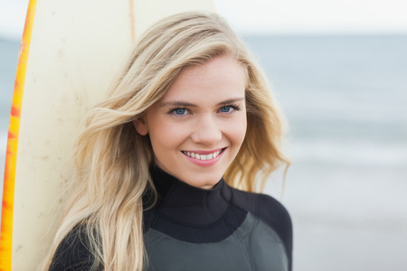 Portrait of a smiling beautiful young woman with surfboard on beachの写真素材