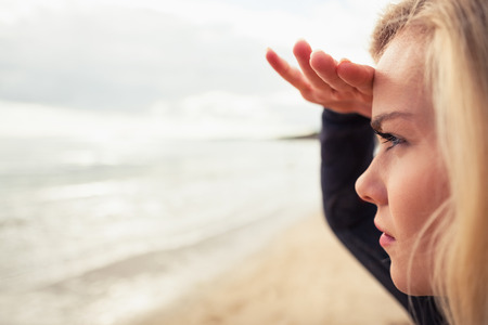 Close up side view of a beautiful blond shielding eyes at the beachの写真素材