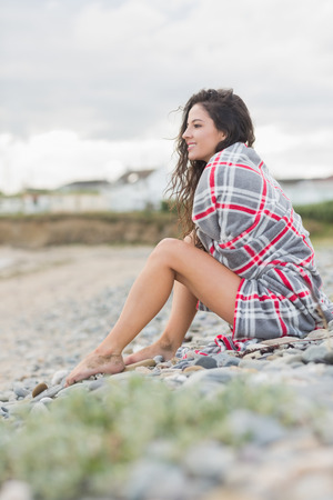 Side view of a smiling young woman covered with blanket at the beachの写真素材