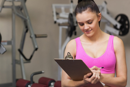 Smiling female trainer writing on clipboard in the gymの写真素材