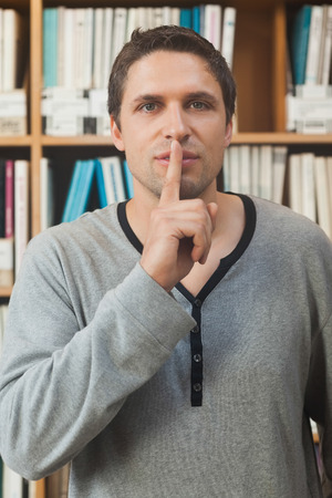 Male librarian making a sign to be quiet in library looking at cameraの写真素材