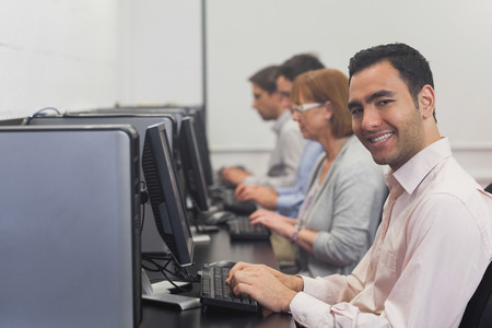 Cheerful mature student sitting in computer class smiling at cameraの写真素材