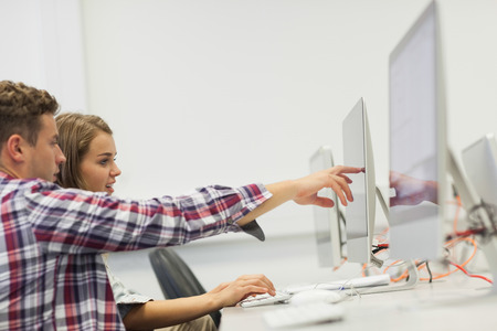 Two students working on computer pointing at it in computer room at college