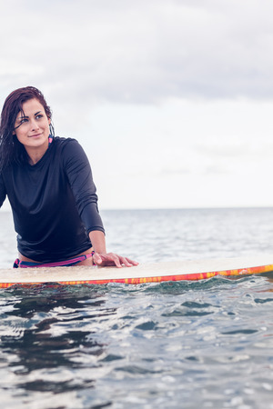 Beautiful young woman with surfboard in the water at beach