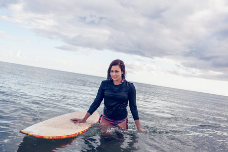 Portrait of a beautiful young woman with surfboard in the water at beach