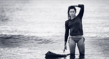 Portrait of a beautiful young woman with surfboard in the water at beach