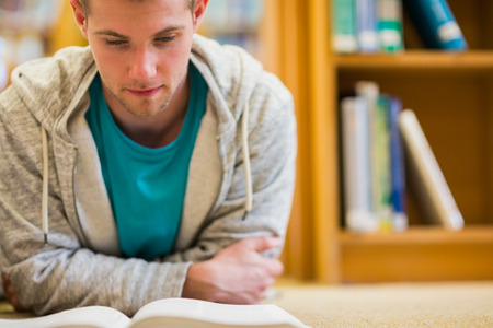Close up of a serious male student reading book on the college library floor