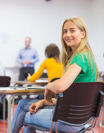 Portrait of a smiling young female student with blurred teachers and others in the classroomの写真素材