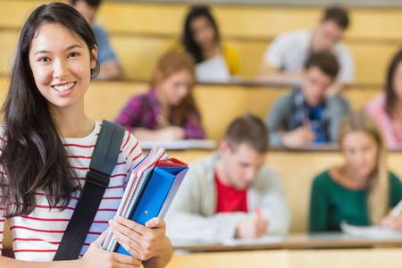 Portrait of a smiling female with students sitting at the college lecture hallの写真素材