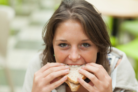 Close up portrait of a smiling female student eating sandwich in the cafeteriaの写真素材
