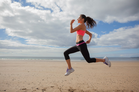 Full length of a healthy young woman jogging on shore at beachの写真素材