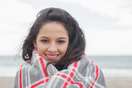 Portrait of a young woman covered with blanket at the beachの写真素材