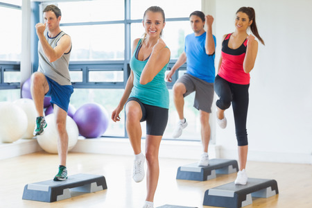 Full length of instructor with fitness class performing step aerobics exercise in gymの写真素材