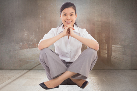 Businesswoman sitting cross legged with hands together against urban projection on wallの写真素材