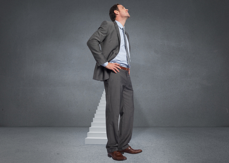 Smiling businessman with hands on hips against steps in grey roomの写真素材