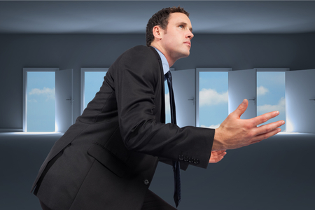 Businessman posing with arms out against doors opening in dark room to show sky の写真素材
