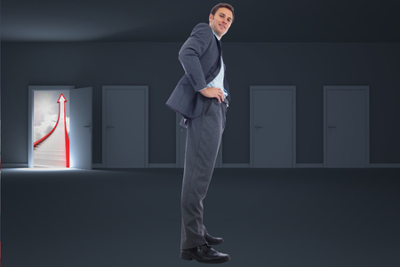 Happy businessman with hands on hips against door opening to show red arrow and skyの写真素材