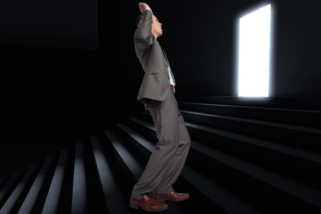 Businessman posing with hands up against steps leading to light in the darknessの写真素材