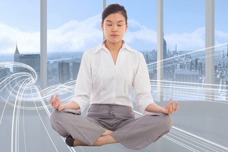 Businesswoman sitting in lotus pose against white design in roomの写真素材