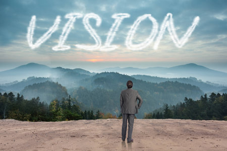 The word vision and businessman with hand on hip against scenic countryside with mountainsの写真素材