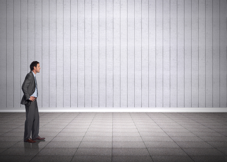 Smiling businessman with hands on hips against grey roomの写真素材