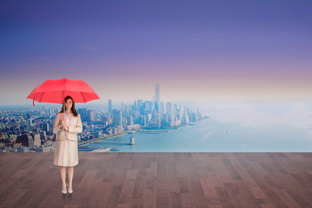 Attractive businesswoman holding red umbrella against city projection on wallの写真素材