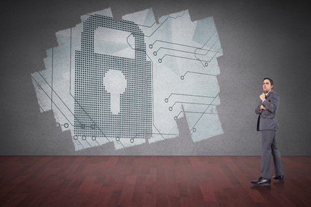 Thoughtful businessman holding pen to chin against display on wall showing digital lockの写真素材