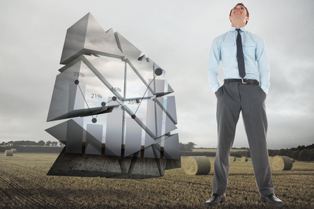 Happy businessman standing with hands in pockets against landscape with bales of strawの写真素材