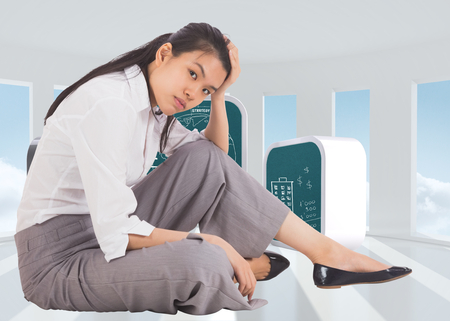 Depressed businesswoman sitting with hand on head against bright white room with windowsの写真素材
