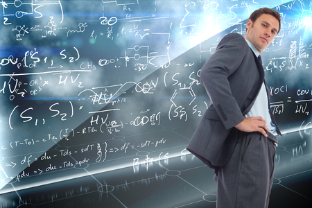 Stern businessman standing with hands on hips against math equation backgroundの写真素材