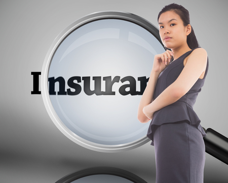 Thinking asian businesswoman against magnifying glass showing insurance wordの写真素材