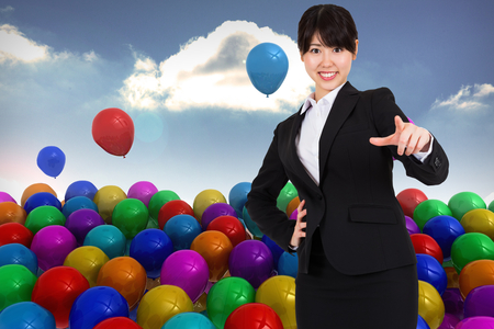 Smiling businesswoman pointing against many colourful balloons sky backgroundの写真素材